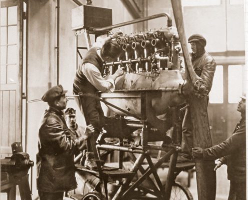 Ein historisches Foto von Ingenieuren, die in einer Werkstatt an einem der ersten Flugzeugmotoren arbeiten.
