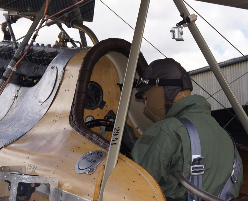 Nahaufnahme des Cockpits eines historischen Doppeldeckerflugzeugs mit einem Piloten, der das Flugzeug steuert.