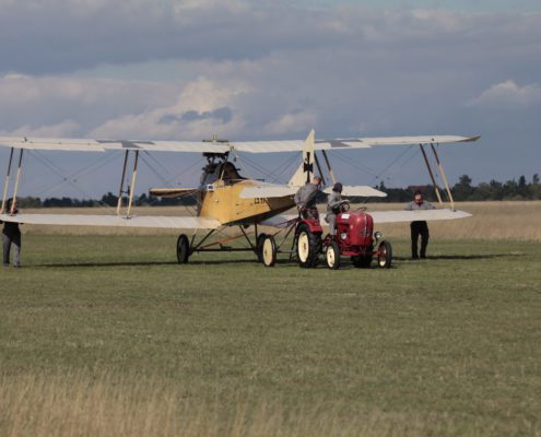 Das Flugzeug steht auf einem offenen Feld und ist mit einem kleinen roten Traktor verbunden, der anscheinend das Flugzeug zieht.