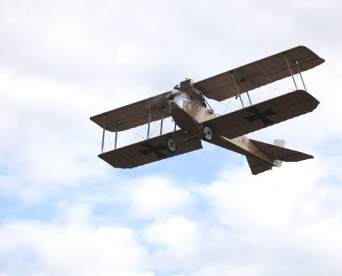 Das Flugzeug im Flug, aus der Perspektive von Boden, gegen einen bewölkten Himmel. Die historischen Markierungen sind deutlich sichtbar.