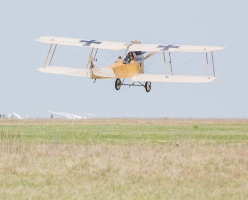 Ein Flugzeug, kurz nach dem Abheben, mit dem Piloten im offenen Cockpit sichtbar mit blauem Himmel